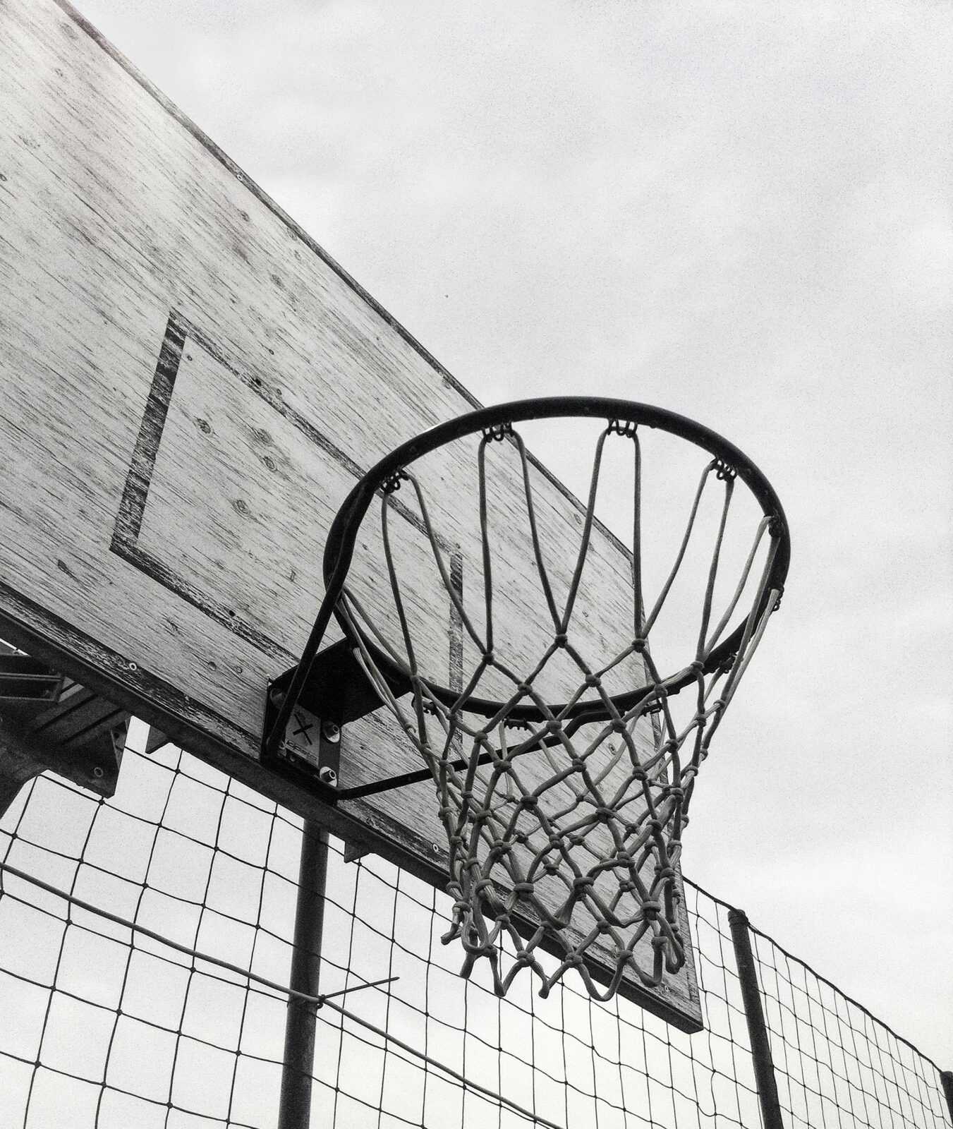 Monochrome shot of a basketball hoop against the sky, capturing the essence of outdoor sports.
