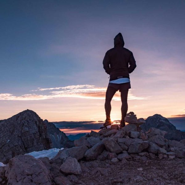Person standing on a rocky mountain peak at sunset in Tolmin, Slovenia, embracing nature's beauty.